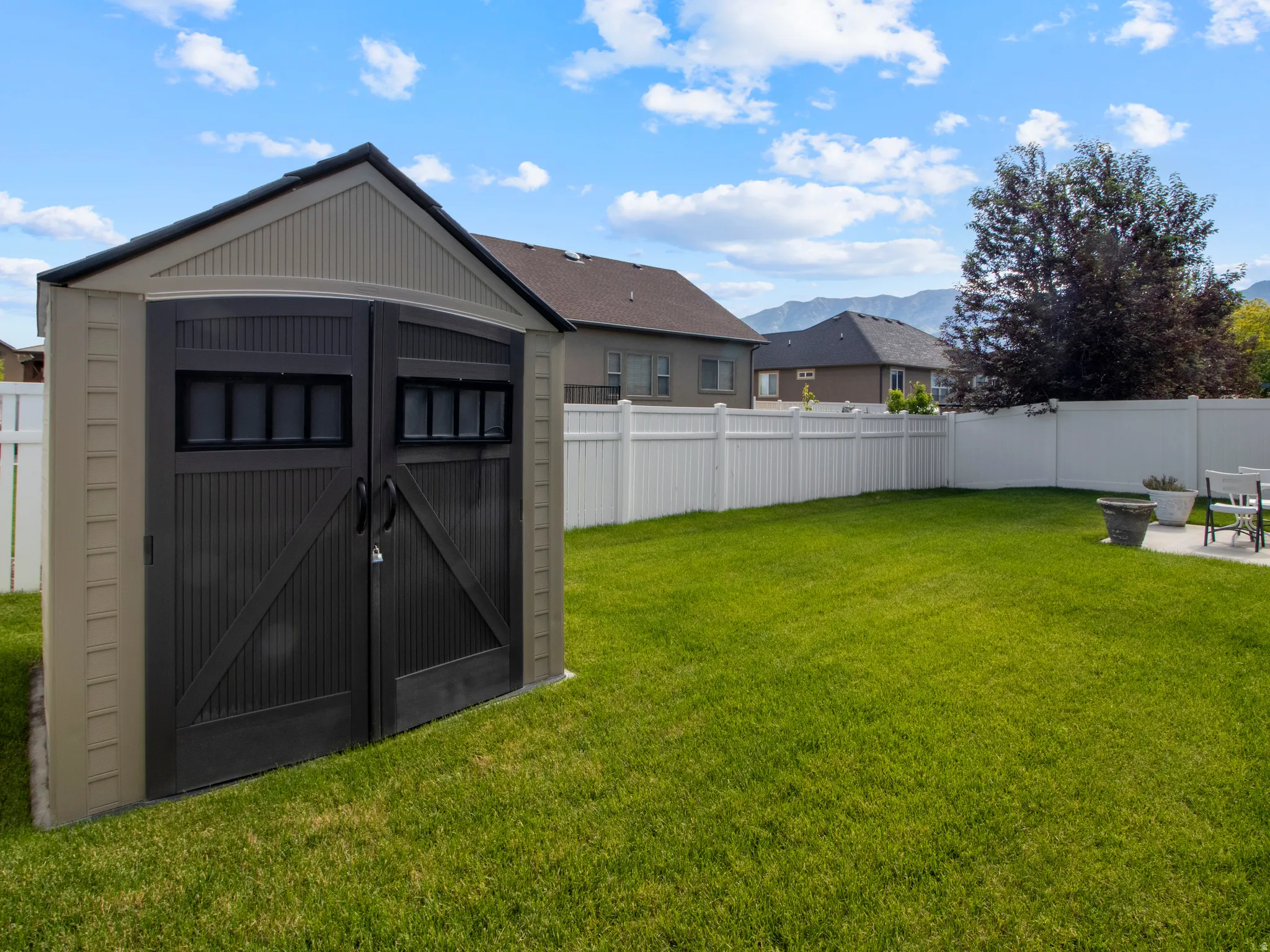 Expansive backyard featuring a lush lawn, white vinyl fencing, and a two-tone storage shed with paneled double doors
