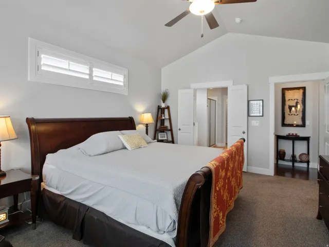 Spacious bedroom featuring vaulted ceilings, a ceiling fan with light, and plantation shutters