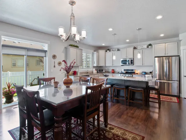 Open-concept kitchen and dining area featuring wood-finish flooring, light gray cabinetry, stainless steel appliances, a center island with bar seating, and a sliding glass door to the exterior