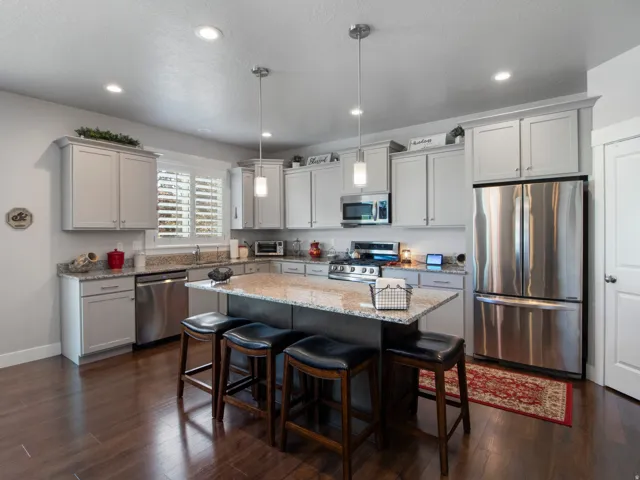Kitchen featuring a center island with bar seating, stainless steel appliances, granite countertops, light gray cabinetry, and dark wood-finish flooring