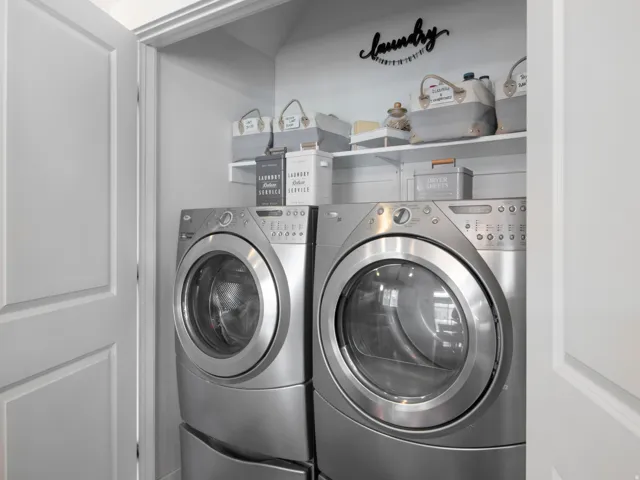 Dedicated laundry closet featuring a stacked washer and dryer, white shelving, and a painted finish