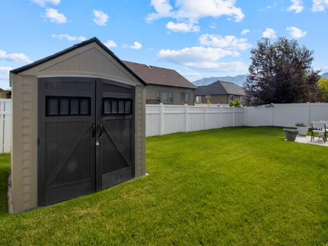 Expansive backyard featuring a lush lawn, white vinyl fencing, and a two-tone storage shed with paneled double doors