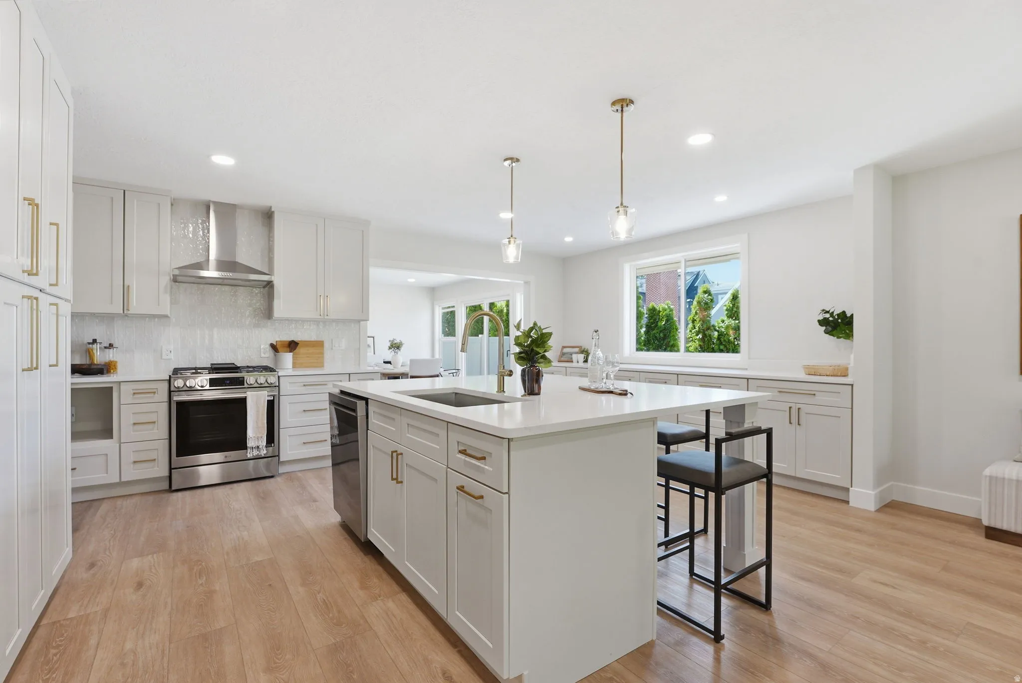 Open-concept kitchen featuring an expansive central island with seating, stainless steel appliances, white shaker cabinetry with gold-tone hardware, wood-finish flooring, and recessed lighting
