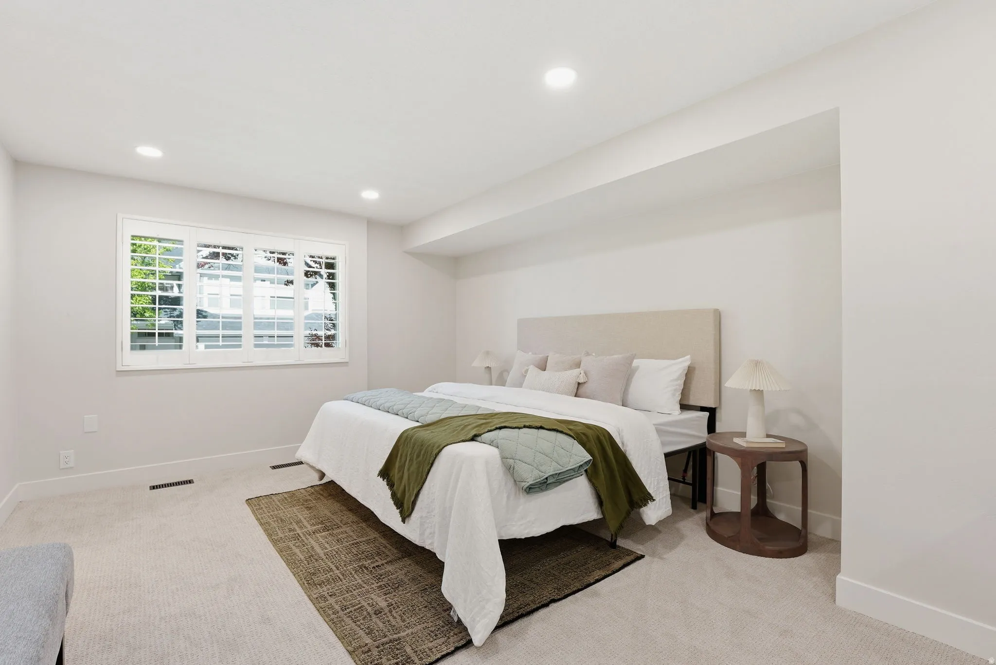 Bedroom featuring a large window with white plantation shutters, neutral-toned carpeting, recessed ceiling lighting, and crisp white baseboards
