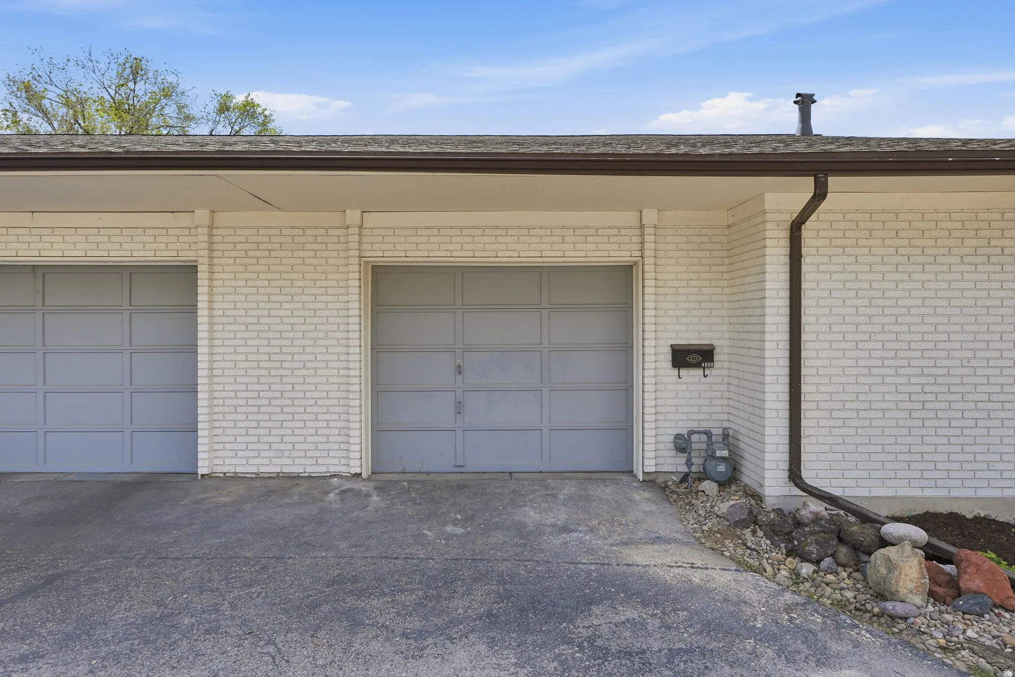 White brick exterior featuring two garage doors, a concrete driveway, and a brown gutter system