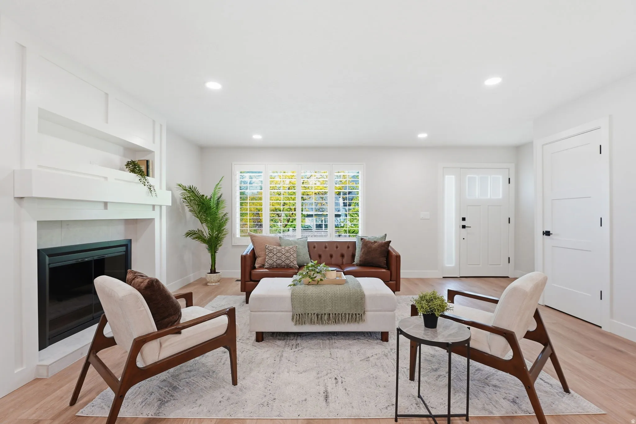 Spacious living area featuring a custom fireplace mantel, recessed lighting, wood-finish flooring, a contemporary entry door with sidelight, and white plantation shutters