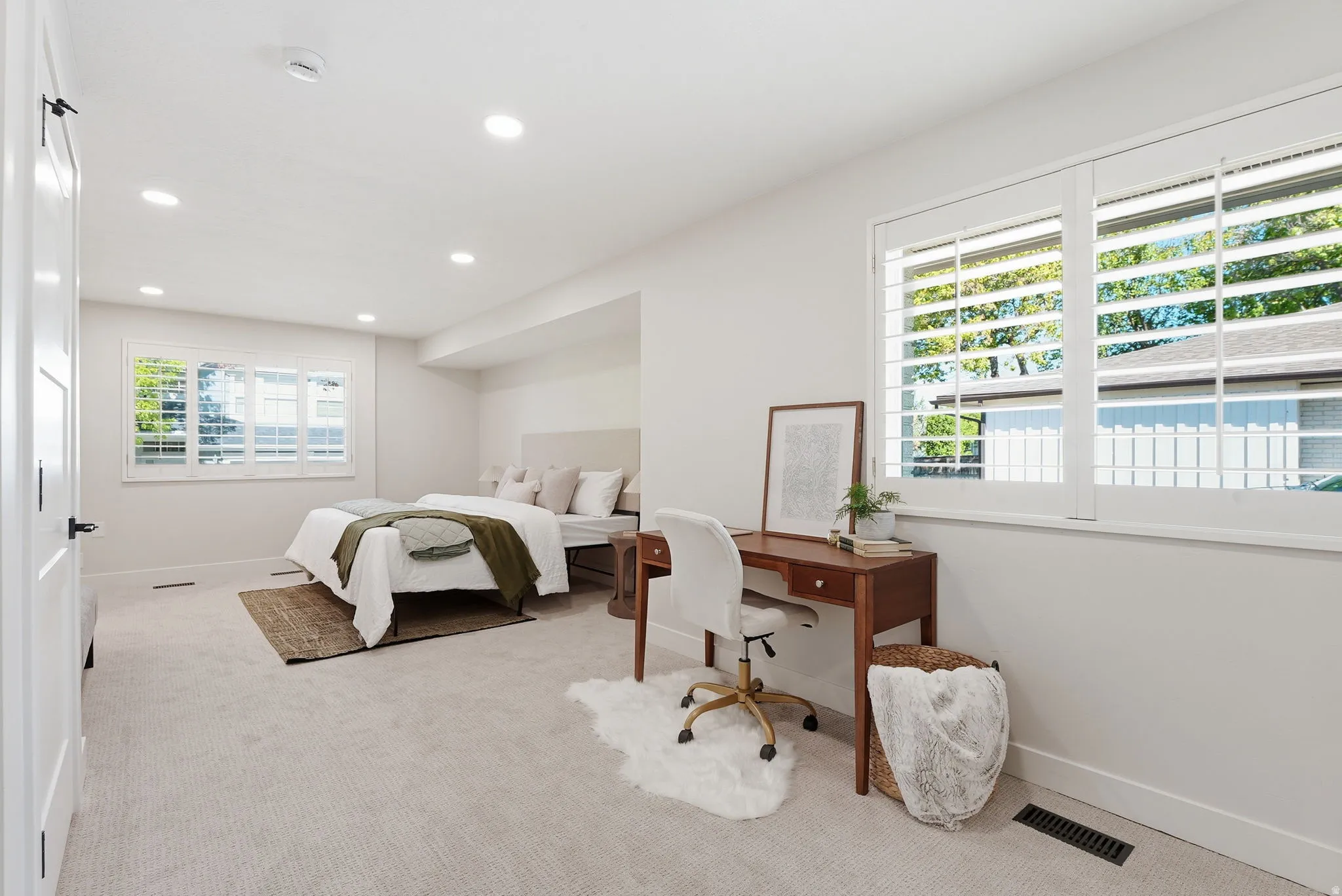 Spacious room featuring light-colored carpeting, multiple recessed lighting fixtures, and two windows with white plantation shutters