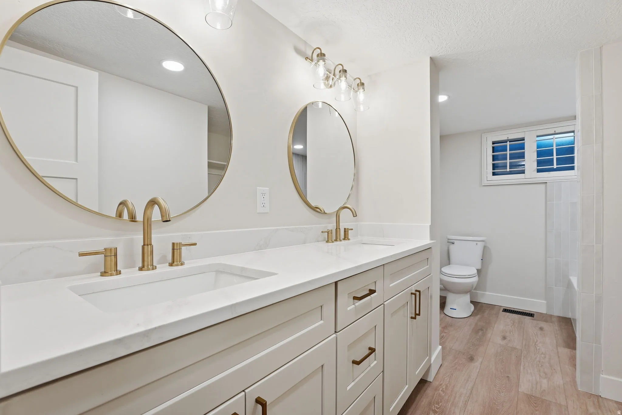 Dual vanity with light-toned cabinetry, gold-toned hardware, and rectangular undermount sinks