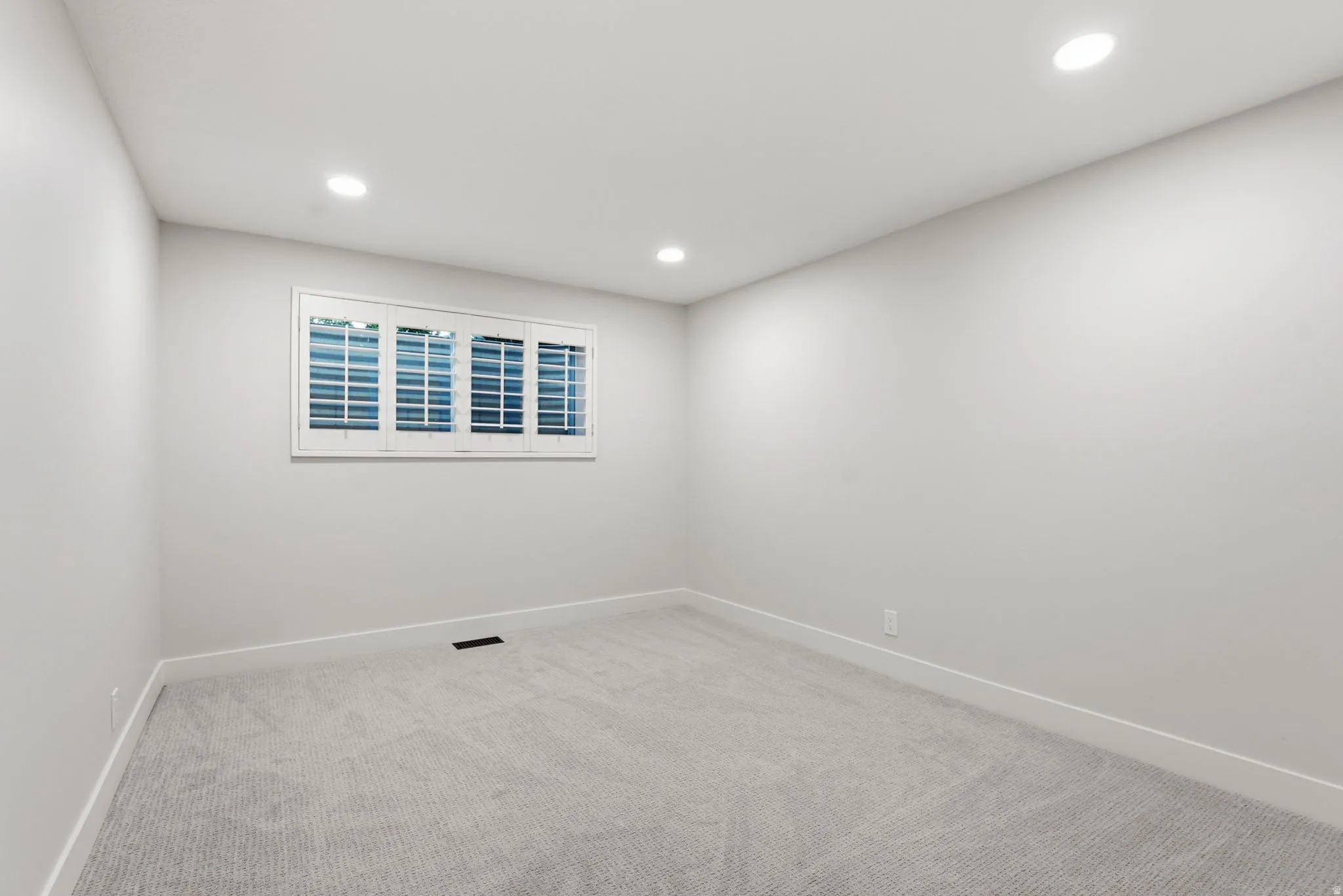 Room featuring light gray carpeting, recessed ceiling lighting, a window with plantation shutters, and white baseboards