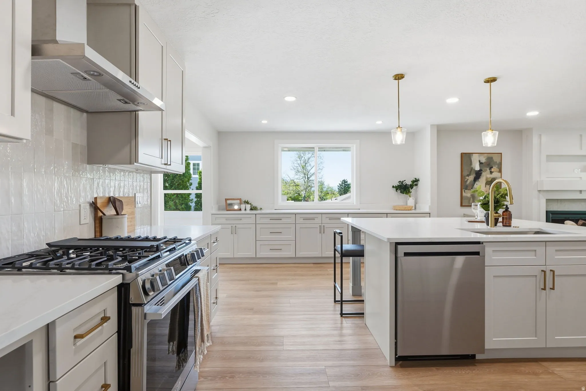 Modern kitchen featuring light wood-finish flooring, white cabinetry with gold-tone hardware, and an island with an integrated stainless steel dishwasher
