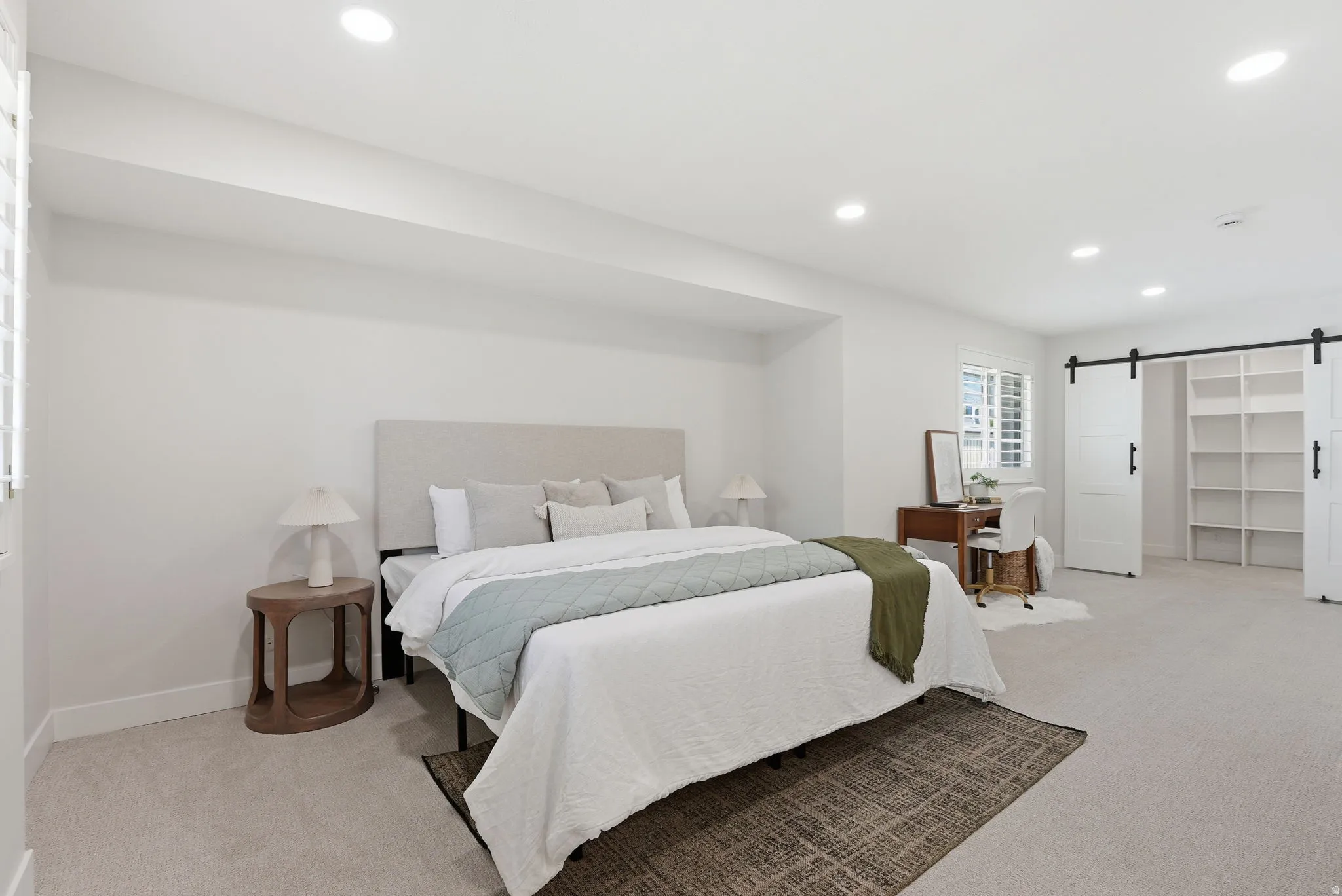 Spacious room featuring neutral carpet flooring, recessed lighting, white plantation shutters, and a built-in shelving unit behind sliding barn doors