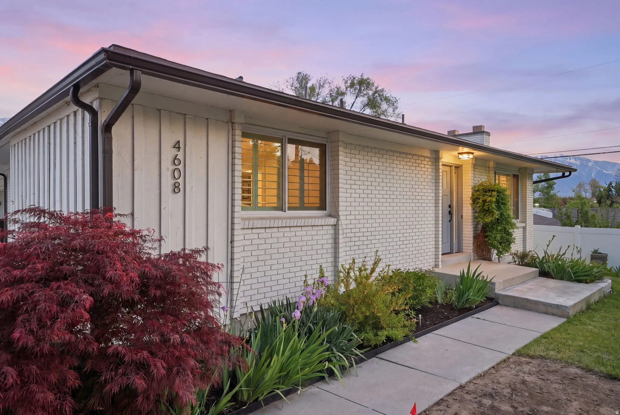 Exterior showcasing light-colored brick and vertical panel siding, dark brown gutters, and a concrete pathway leading to the front entry