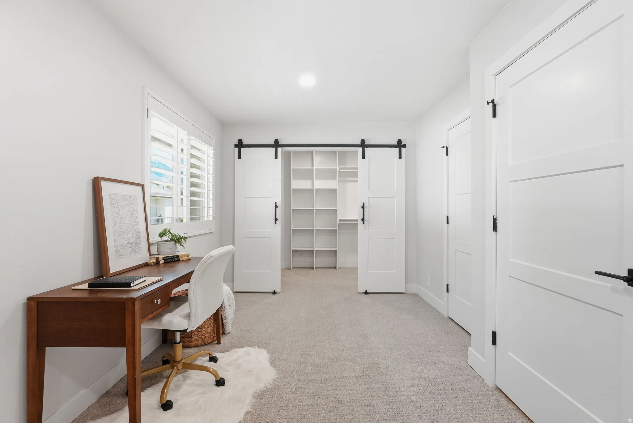 Carpeted room featuring a window with plantation shutters, a barn door entry to a closet with built-in shelving, recessed lighting, and white paneled doors with black hardware