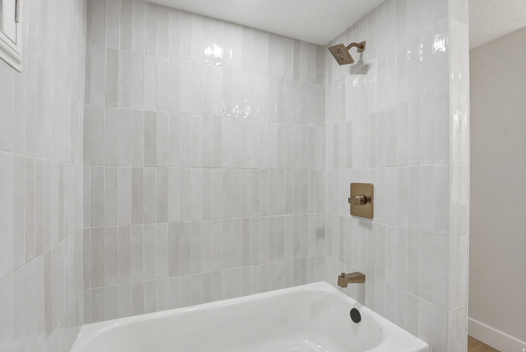 Bathtub with a white finish, vertical stacked tile surround, and bronze-finish fixtures