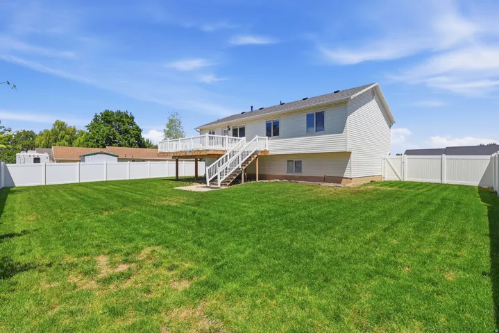 Spacious backyard featuring a manicured lawn, full perimeter white vinyl fencing, and a multi-level deck with stairs to grade