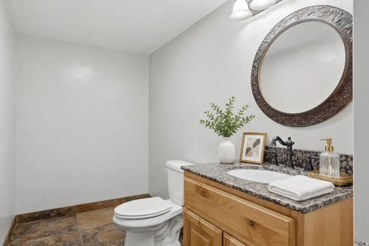 Vanity with light wood-finish cabinetry, stone countertop, undermount sink, and black-finish faucet