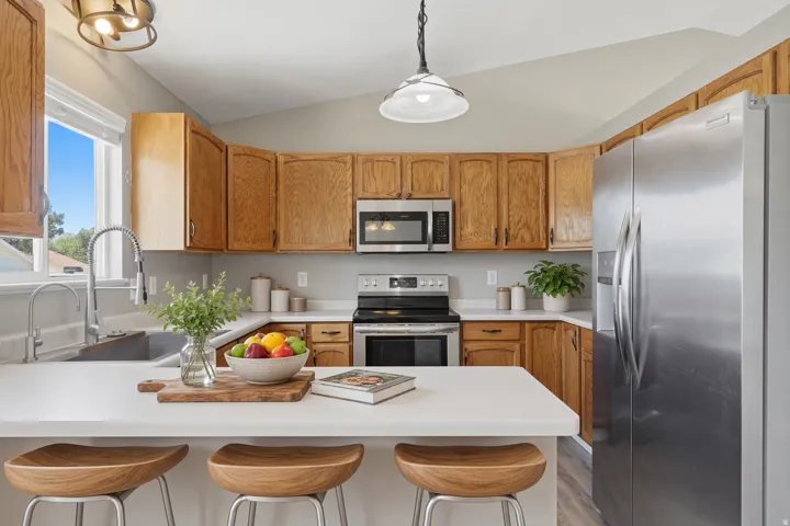 Kitchen featuring wood cabinetry, stainless steel appliances, white countertops, a kitchen island, and vaulted ceilings