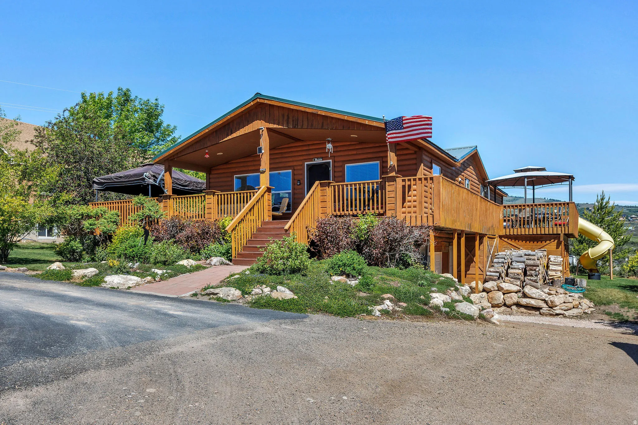 Log cabin exterior featuring a covered front porch, expansive wood decking, and mature landscaping