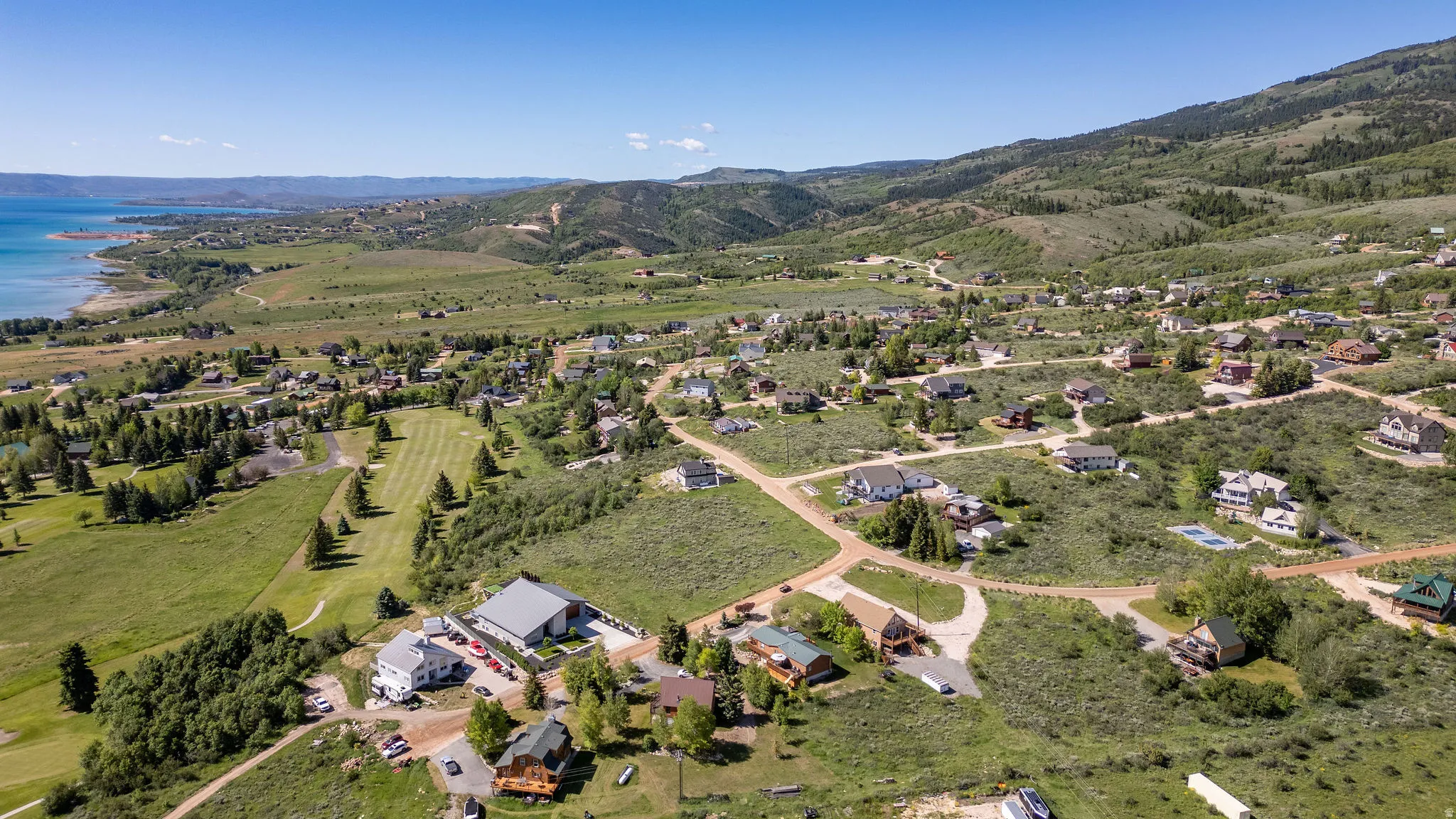 Expansive aerial perspective showcasing a residential community with a large body of water, green hills, and mountainous terrain