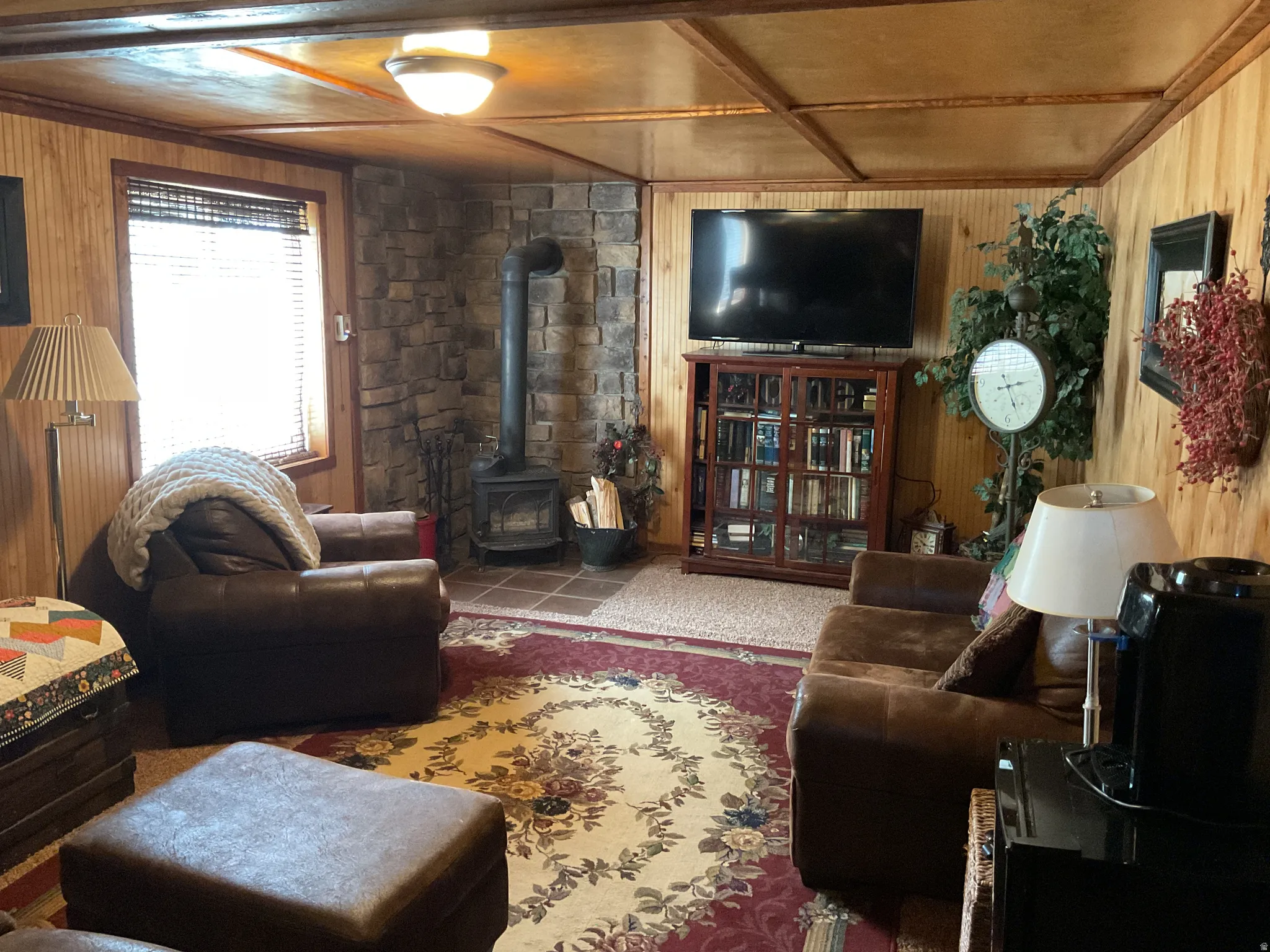 Living area featuring wood-finish paneling, a stone-clad corner, and a freestanding wood-burning stove