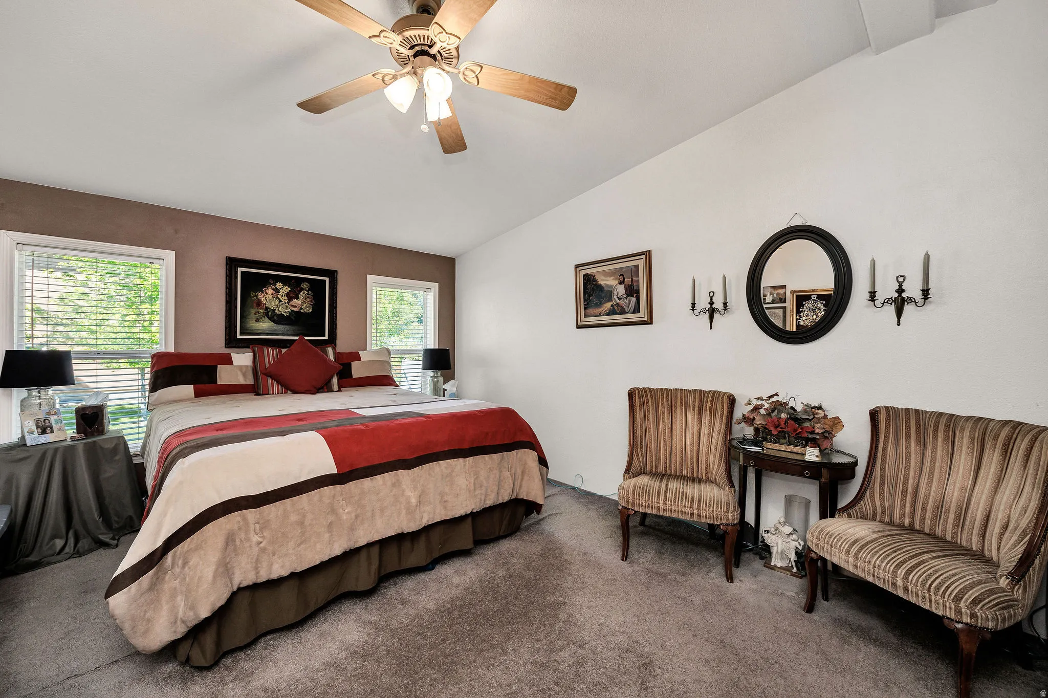 Spacious room featuring vaulted ceilings, carpet flooring, a ceiling fan with integrated lighting, and two large windows with blinds