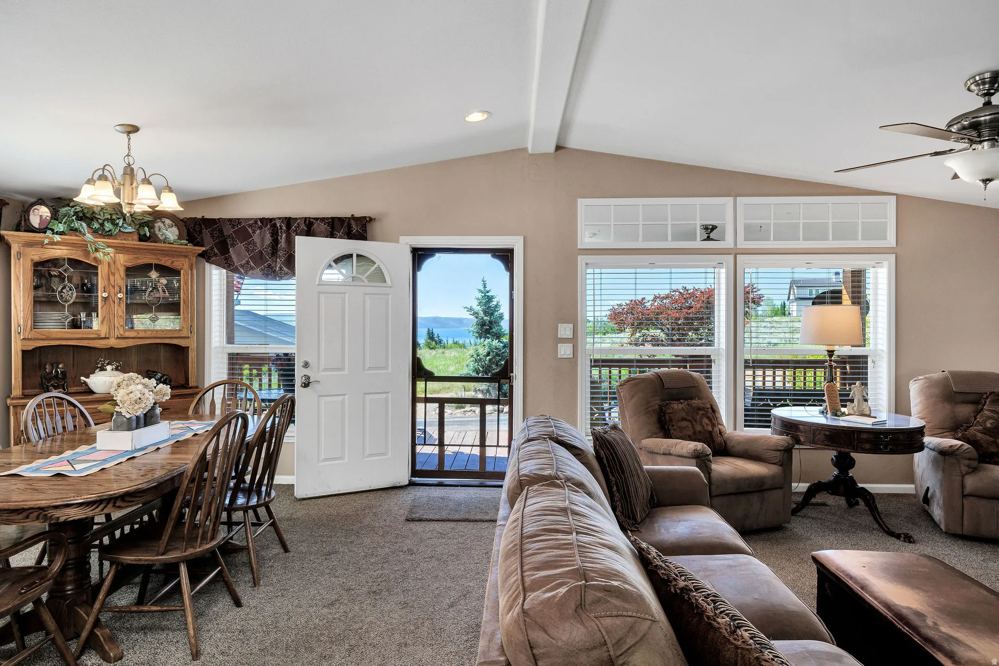 Vaulted ceiling living area with a ceiling fan, carpet flooring, and abundant natural light from multiple windows