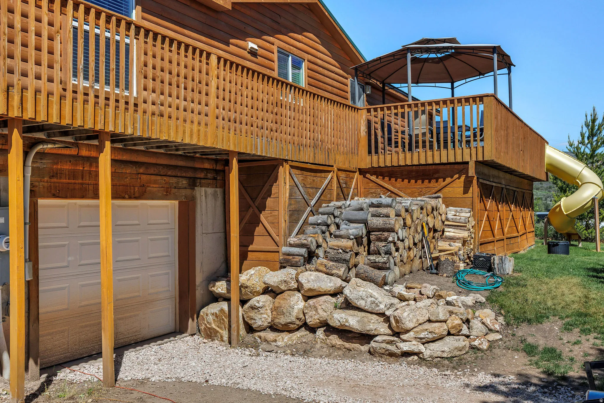 Wood-sided exterior featuring a two-story wood deck with railings, an attached gazebo, and a yellow tube slide