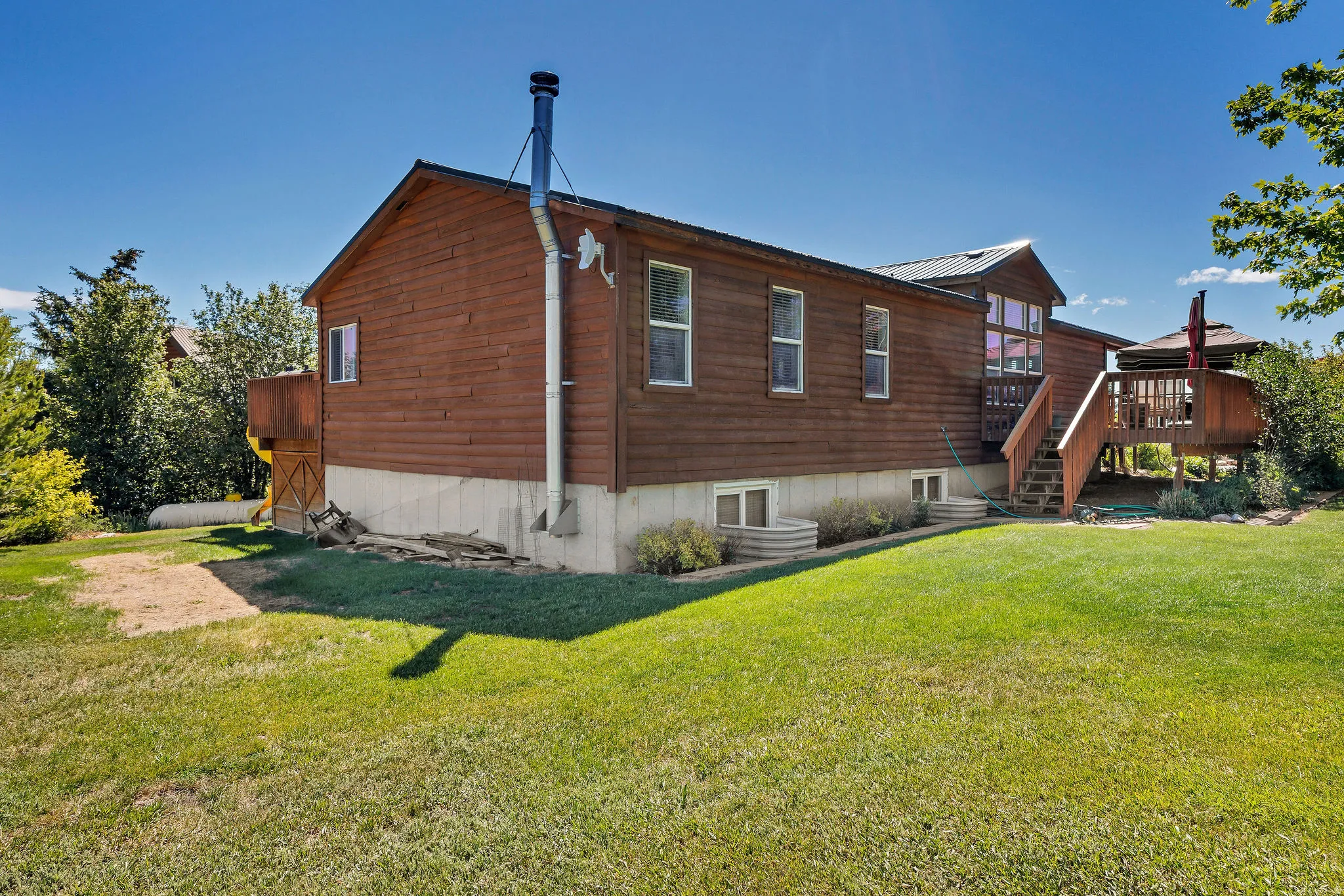 Wood-sided property with a visible foundation, featuring a large exterior deck with wooden stairs