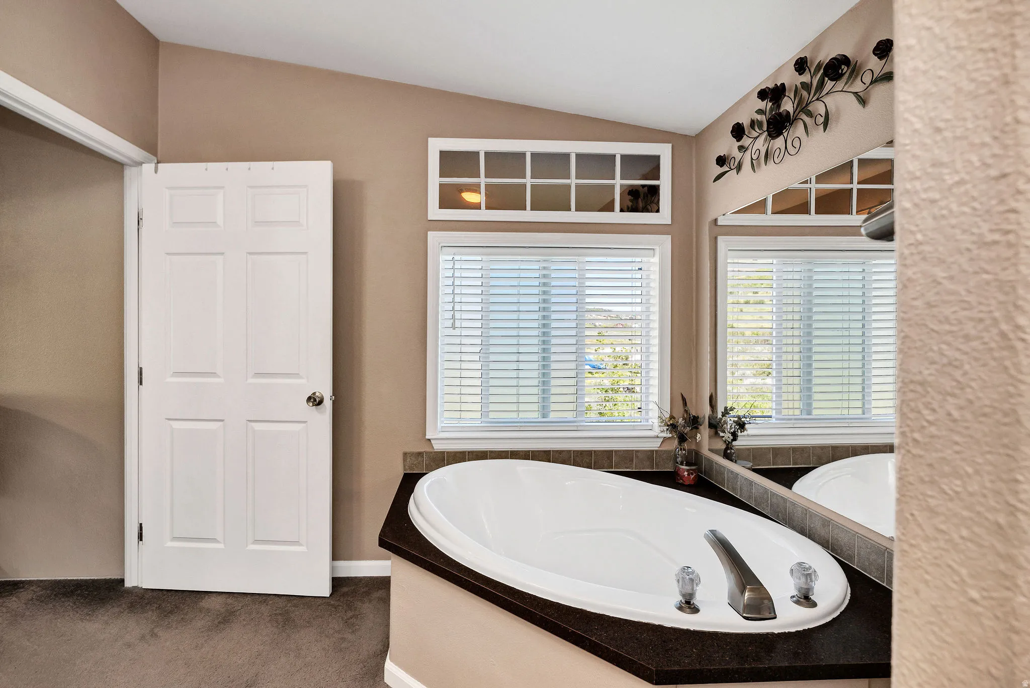 Soaking tub with dark countertop surround, framed by two windows with blinds