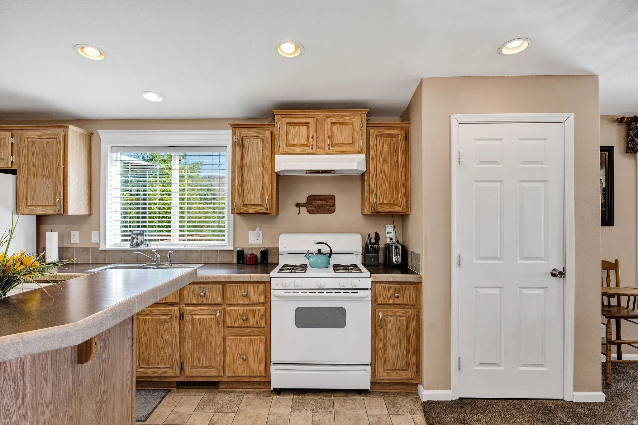 Kitchen featuring light wood cabinetry, a built-in oven with overhead range hood, recessed lighting, and a window with blinds