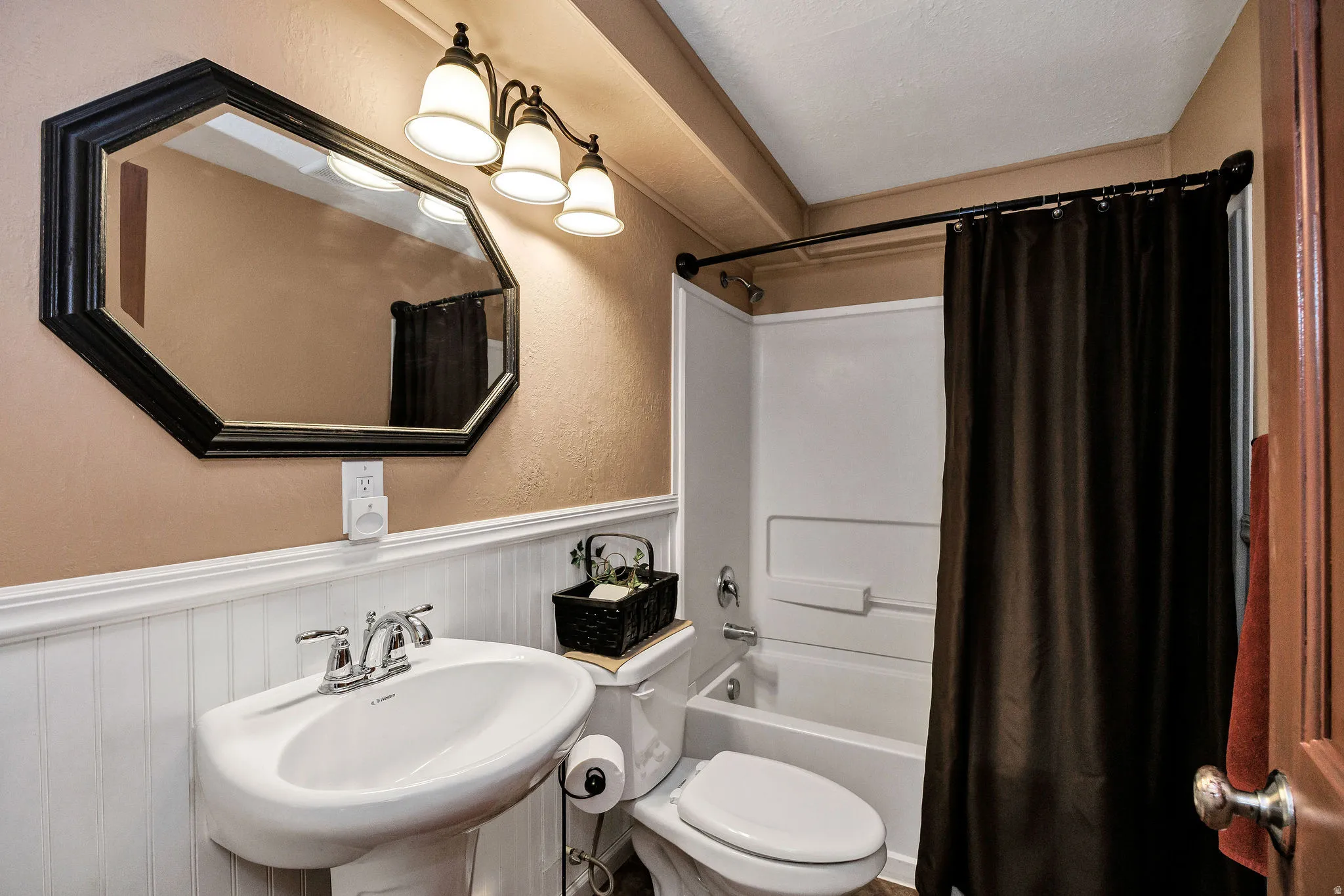 Bathroom featuring a white pedestal sink with chrome faucet, a wall-mounted octagonal mirror, and a three-light vanity fixture