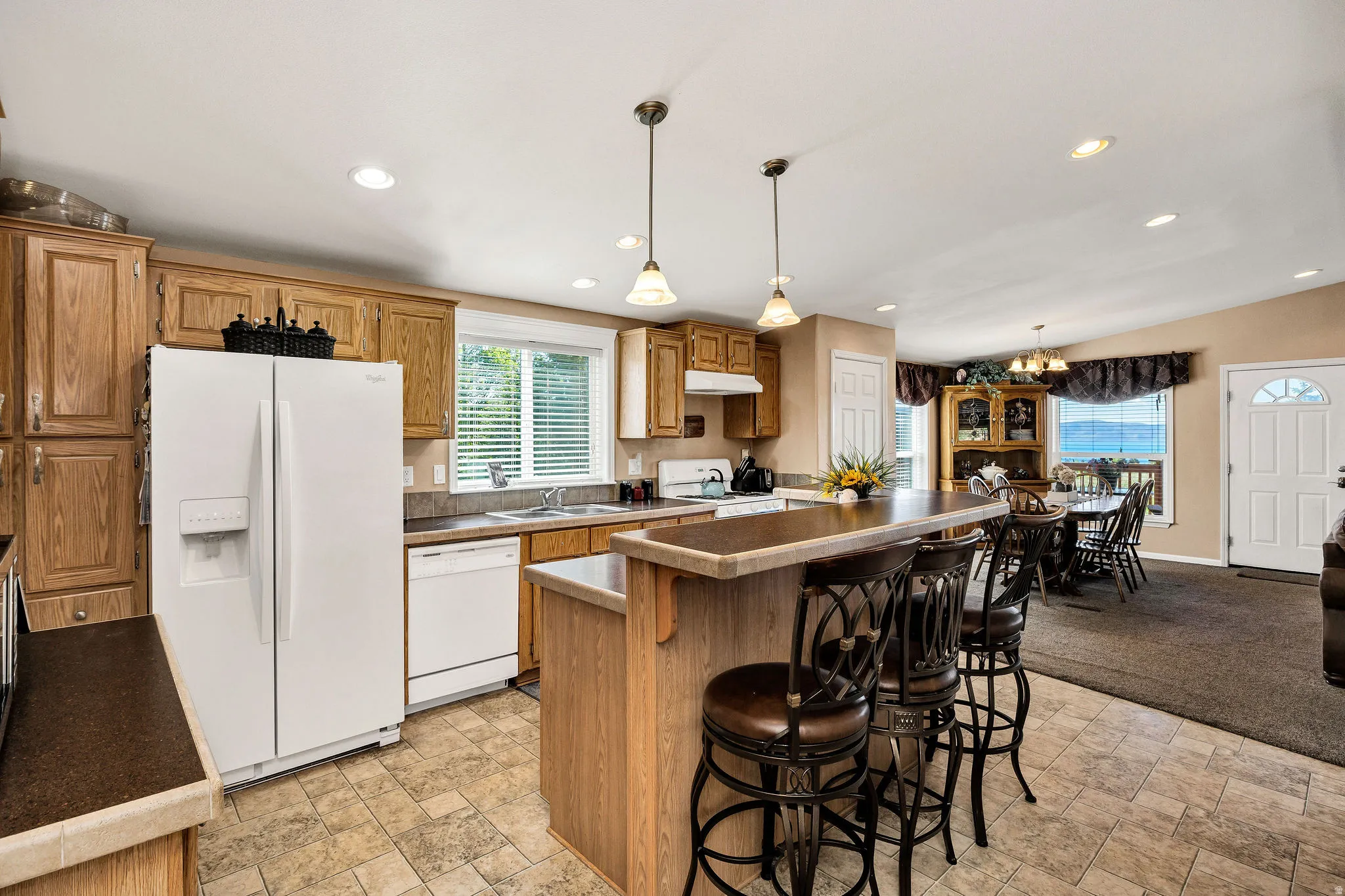 Kitchen featuring wood cabinetry, white appliances, and a central island with bar seating