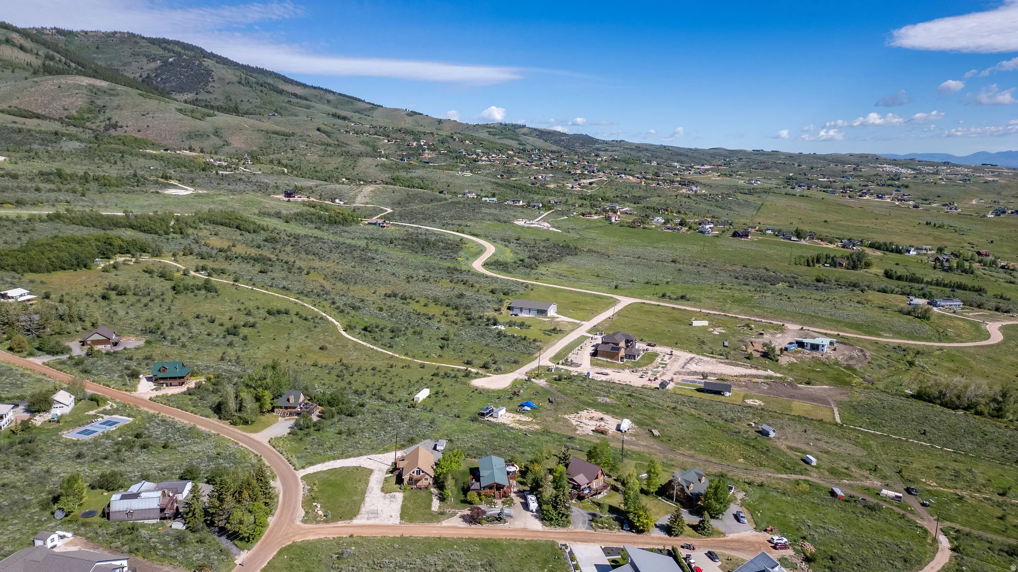 Expansive rural landscape featuring rolling hills and scattered residences under a clear blue sky