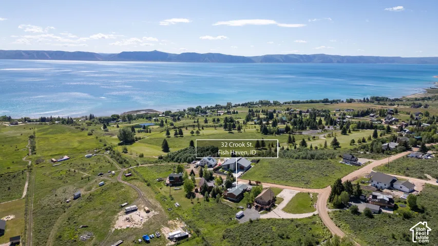 Aerial perspective showcasing a property in a waterside community, featuring a large body of water, expansive green spaces, surrounding mountainous terrain, and clustered residential structures