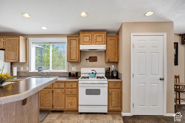 Kitchen featuring light wood cabinetry, a built-in oven with overhead range hood, recessed lighting, and a window with blinds