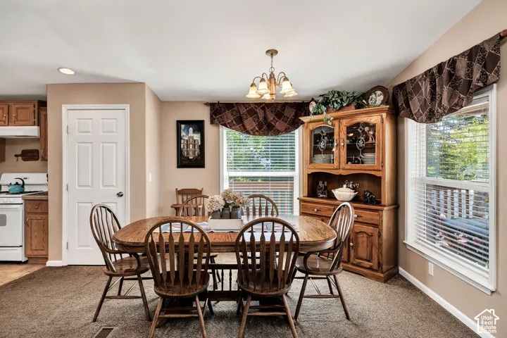 Carpeted dining area featuring a chandelier, two windows with blinds, and a built-in hutch with glass-fronted upper cabinets