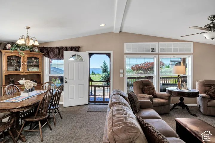 Vaulted ceiling living area with a ceiling fan, carpet flooring, and abundant natural light from multiple windows