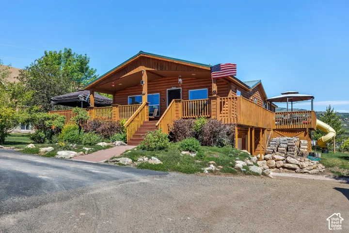 Log cabin exterior featuring a covered front porch, expansive wood decking, and mature landscaping