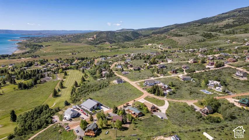 Expansive aerial perspective showcasing a residential community with a large body of water, green hills, and mountainous terrain