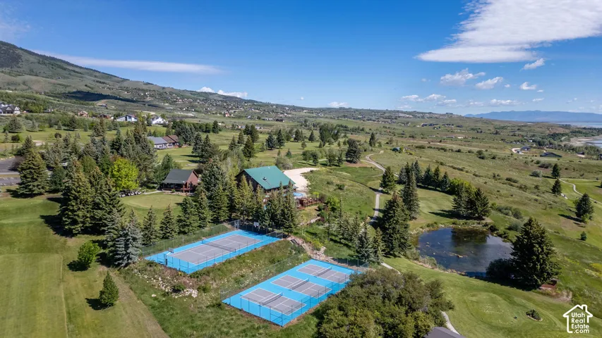 Aerial perspective revealing multiple tennis courts with blue surfaces, a green-roofed structure, and a circular pond