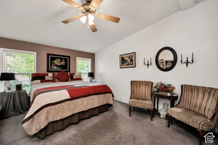 Spacious room featuring vaulted ceilings, carpet flooring, a ceiling fan with integrated lighting, and two large windows with blinds