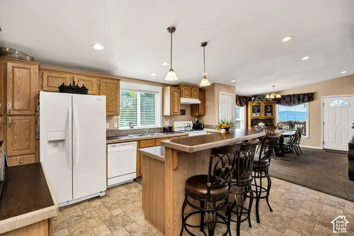 Kitchen featuring wood cabinetry, white appliances, and a central island with bar seating