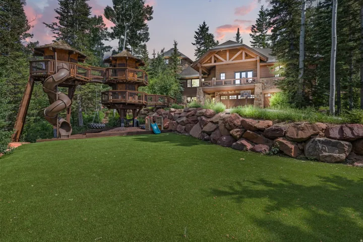 Expansive synthetic turf lawn with a multi-level wooden play structure featuring slides and elevated platforms