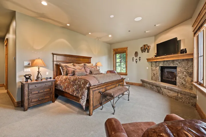 Carpeted room featuring a stone fireplace with a wood mantle, recessed lighting, and multiple windows with wood trim