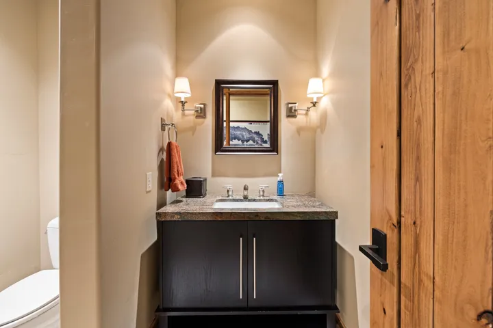 Powder room featuring a dark wood vanity with a stone-finish countertop and integrated sink, framed mirror, and wall sconces