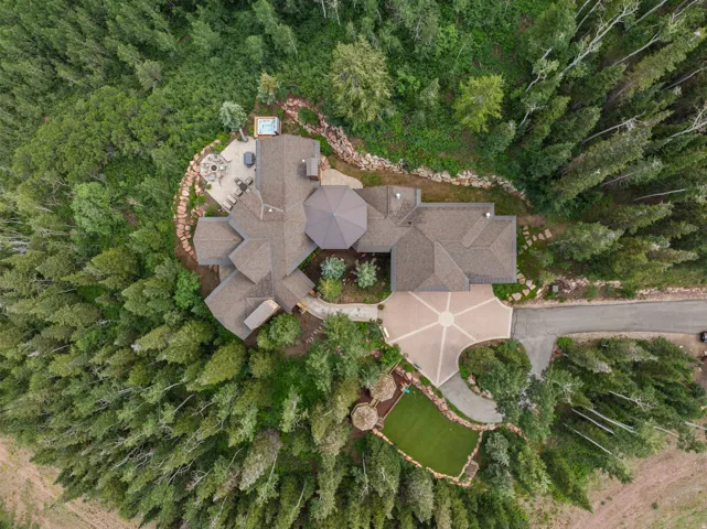 Expansive property featuring a multi-gabled roofline, a large paved driveway with a central design element, a stone patio, and a built-in outdoor spa