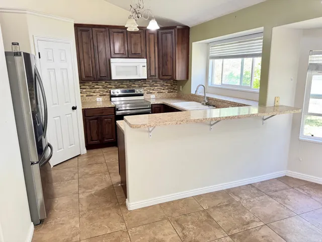 Kitchen featuring granite countertops, wood cabinetry, stainless steel appliances, a tiled backsplash, and tile flooring