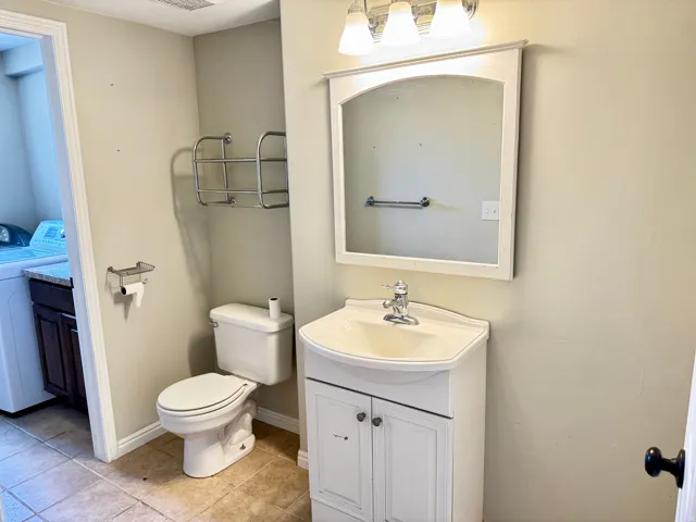Bathroom featuring a white vanity with integrated sink, chrome faucet, wall-mounted mirror, and overhead vanity lighting