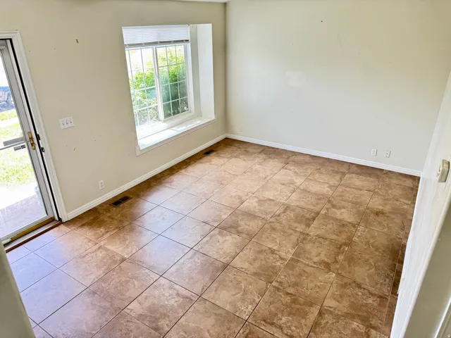 Spacious room featuring neutral-toned walls, large square tile flooring, and a window with a deep sill