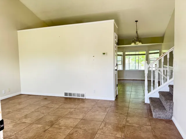 Spacious interior featuring tile flooring, vaulted ceilings, a carpeted staircase with a white baluster railing, and a dining area with a multi-pane bay window